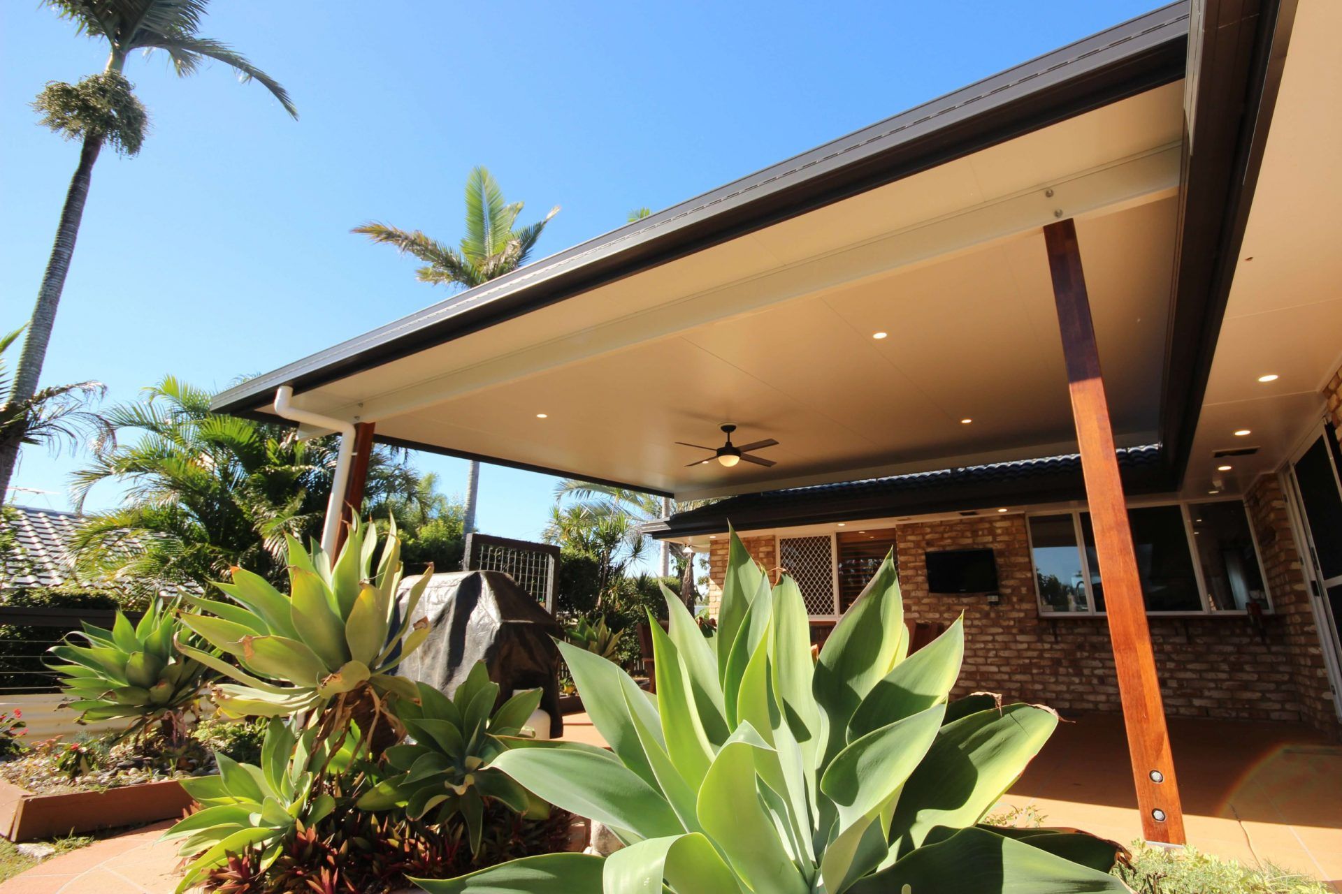 Insulated patio roof with timber posts opening onto a tropical garden